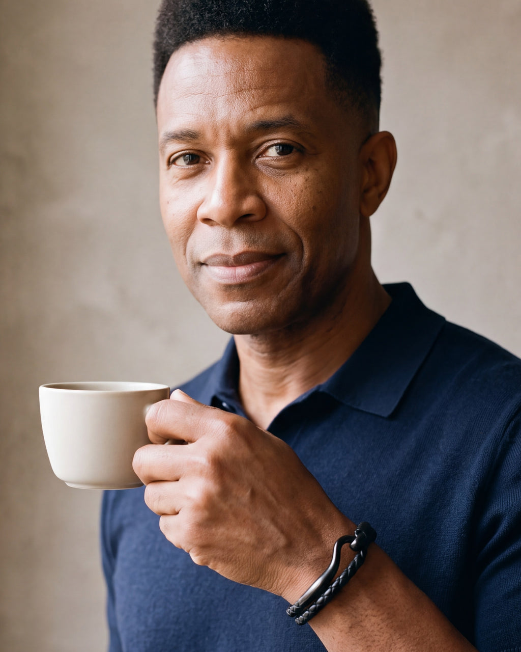 Man in a navy knit polo holding a coffee cup, wearing the black Atlas curved hook leather bracelet