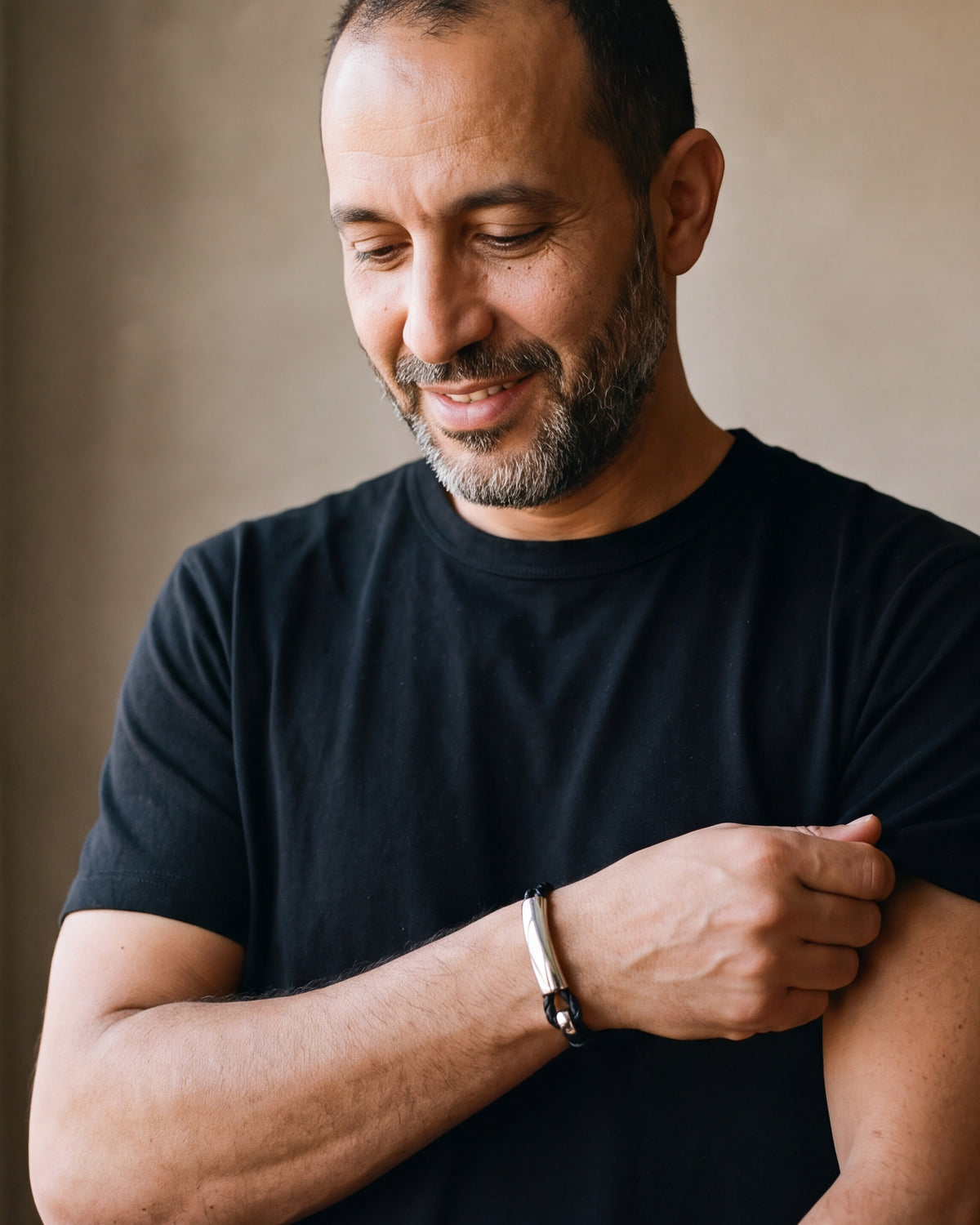 Man in a black t-shirt adjusting his sleeve, wearing the silver Atlas curved hook leather bracelet