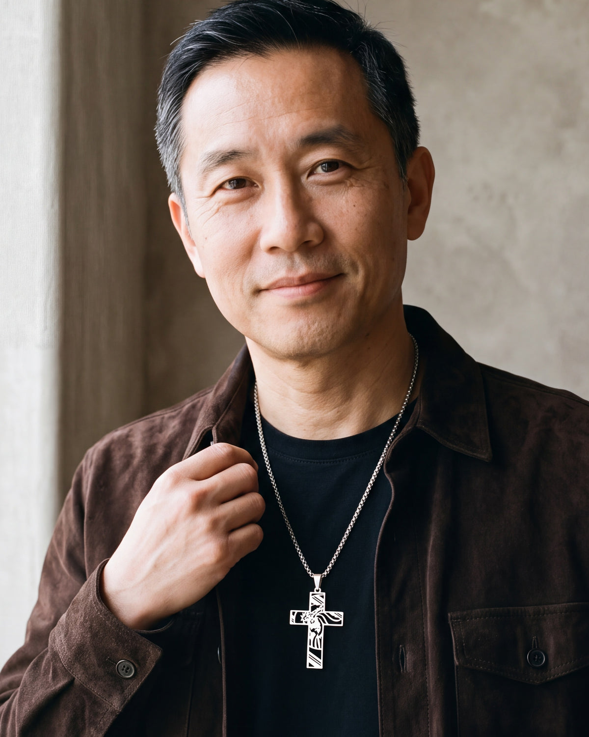 Man in a brown suede overshirt with his hand at the collar, wearing the silver Atlas cut-out cross pendant