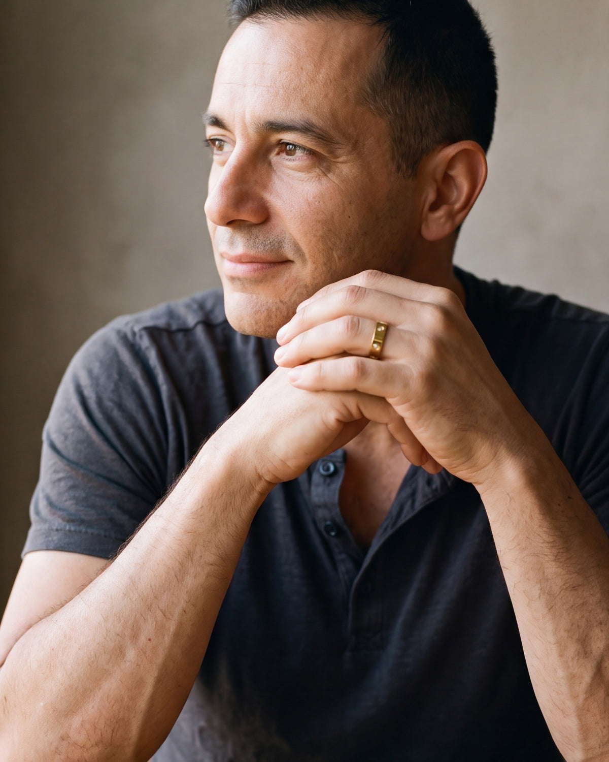 Man in a charcoal henley seated with his hands together, wearing the gold-tone Atlas cubic zirconia band ring