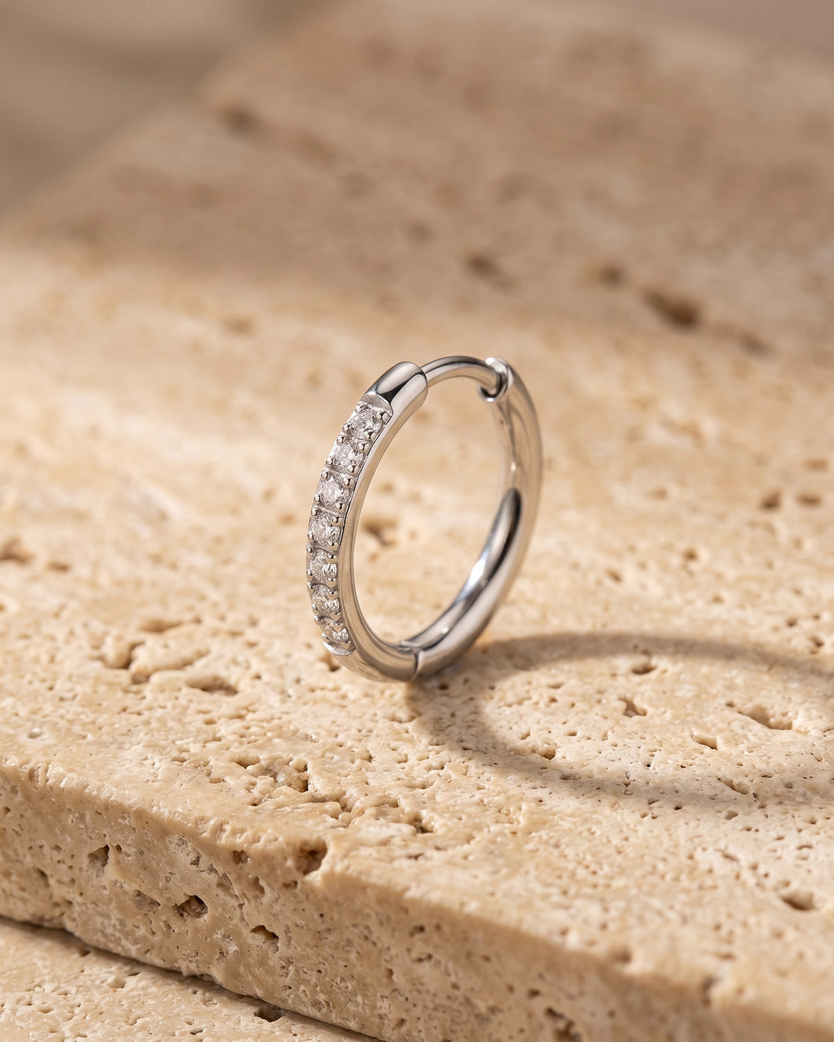Silver Atlas cubic zirconia hoop earring standing on warm stone