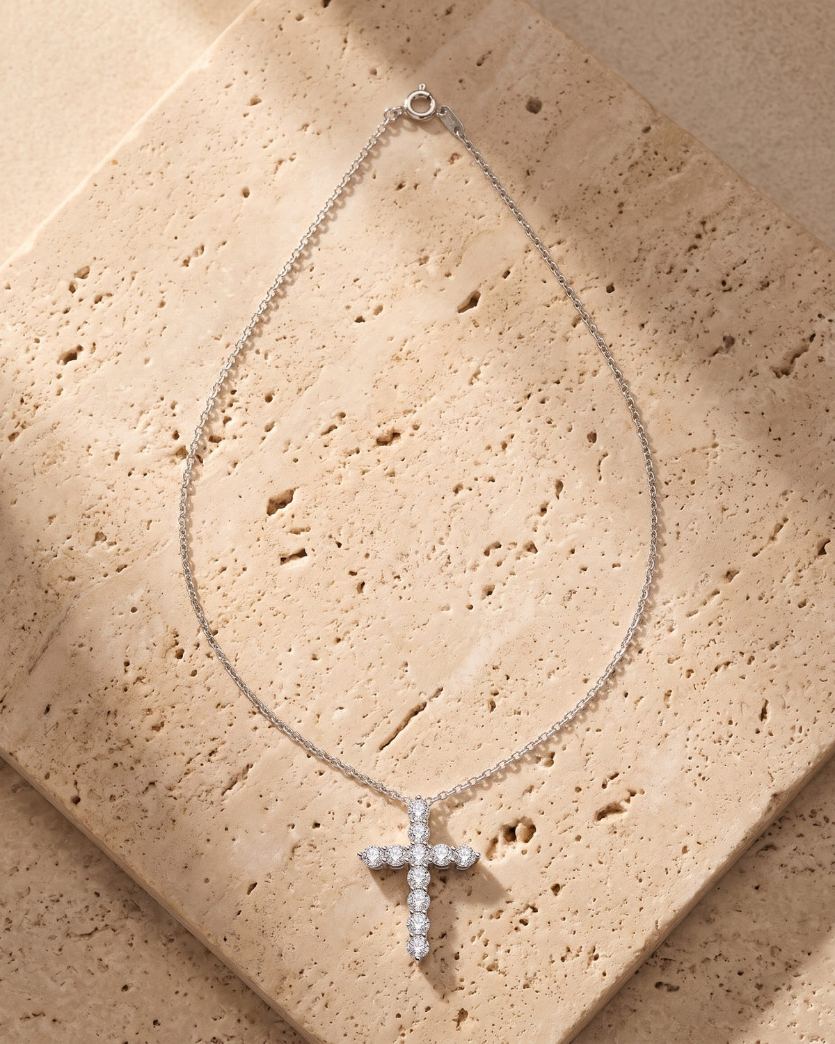 The silver Atlas CZ Cross Necklace in Titanium Steel laid on warm travertine stone