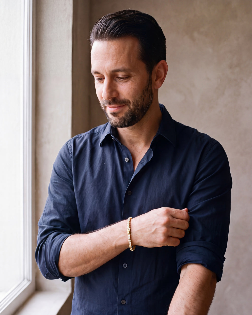 Man in a navy open-collar shirt by a window wearing the gold-tone Atlas CZ tennis bracelet
