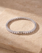 The whole silver Atlas CZ tennis bracelet closed, lying on warm stone