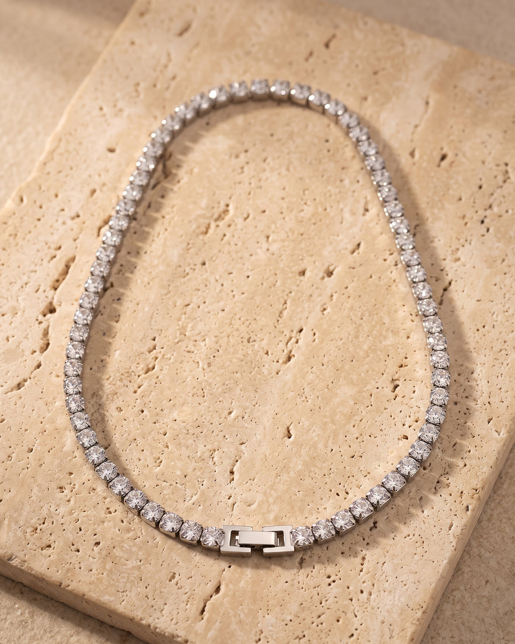 The whole silver Atlas CZ tennis chain laid on warm stone, box clasp closed
