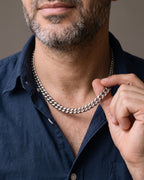 Hand lifting the Atlas Dense Cuban Link Chain in Silver-Tone Steel at the collarbone