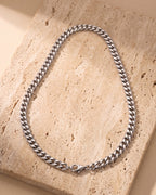 The silver Atlas Dense Cuban Link Chain in Silver-Tone Steel laid on warm travertine stone