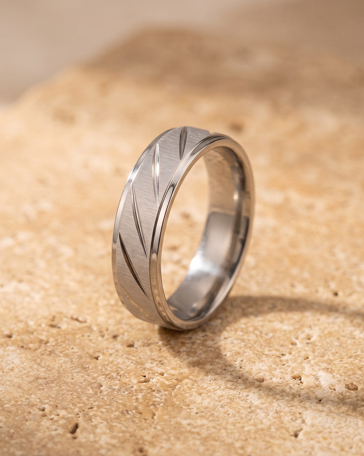 Entire Atlas diagonal cut geometric ring in silver-tone steel, lying flat on warm stone