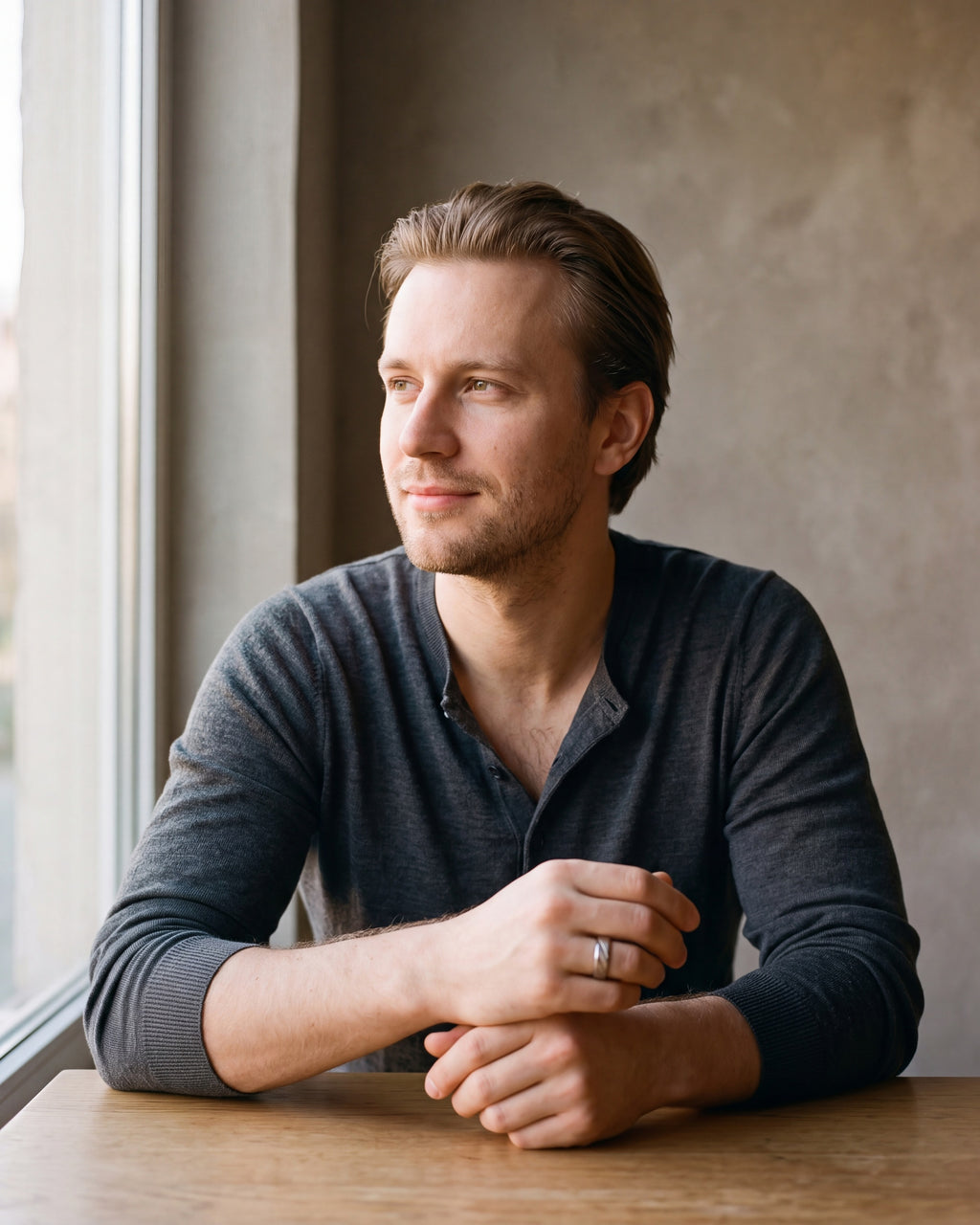 Man in a charcoal knit henley by a window wearing the Atlas diagonal cut geometric ring in silver-tone steel