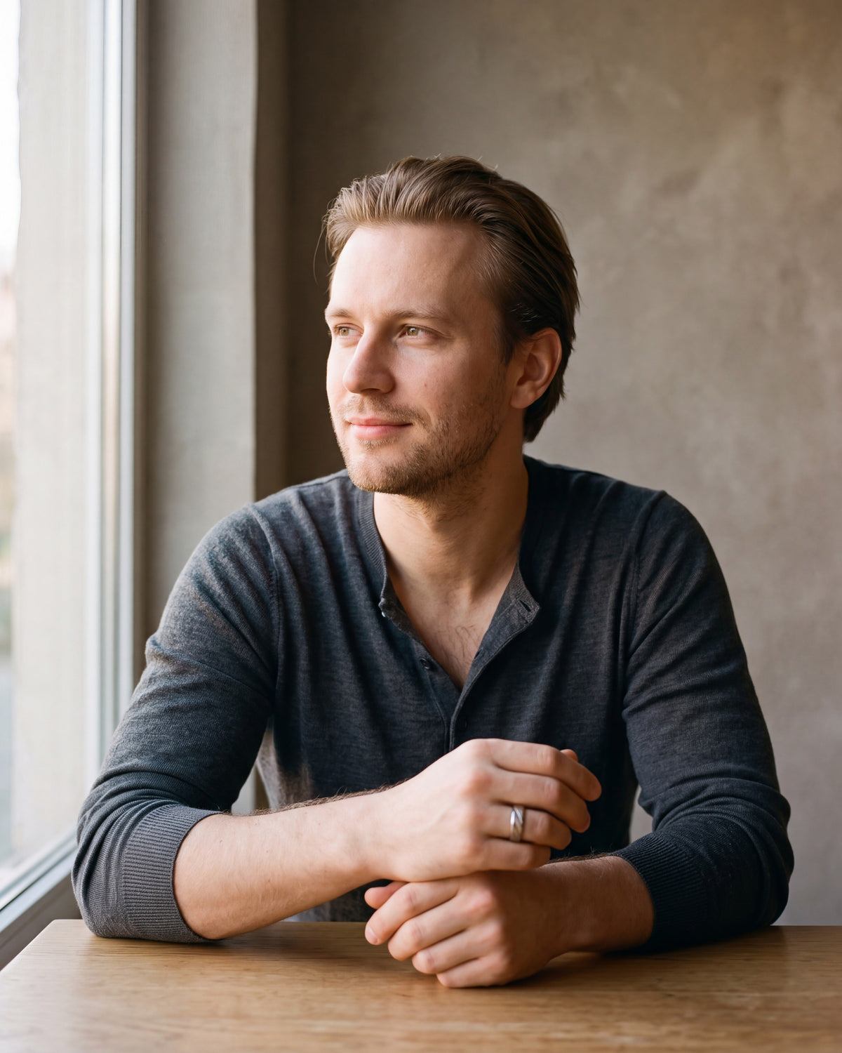 Man in a charcoal knit henley by a window wearing the Atlas diagonal cut geometric ring in silver-tone steel