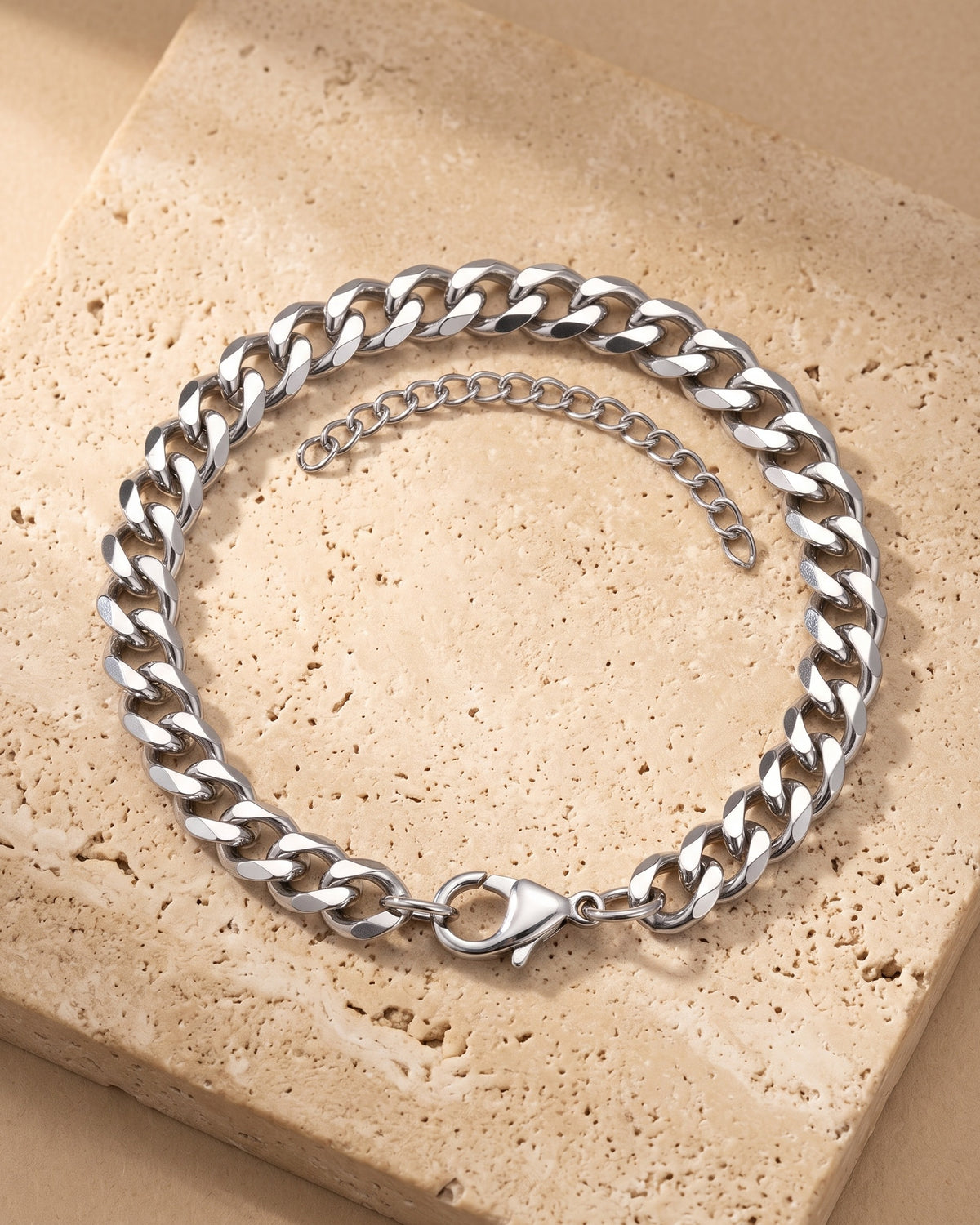 The whole silver-tone Atlas Diamond-Cut Cuban Bracelet lying on warm travertine stone