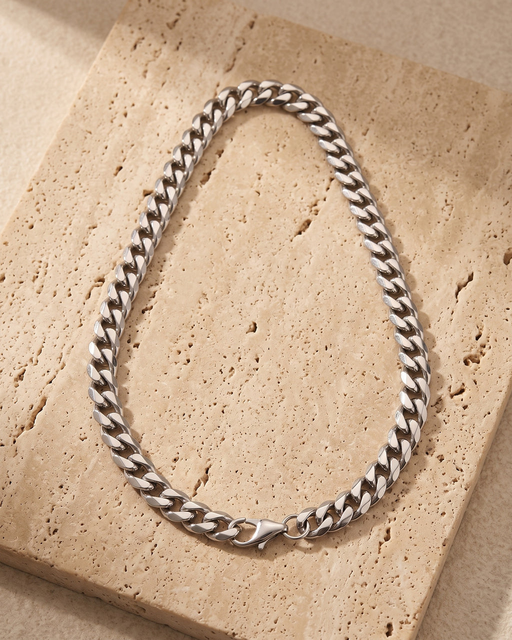 The whole silver Atlas Diamond-Cut Cuban Chain lying on warm travertine stone
