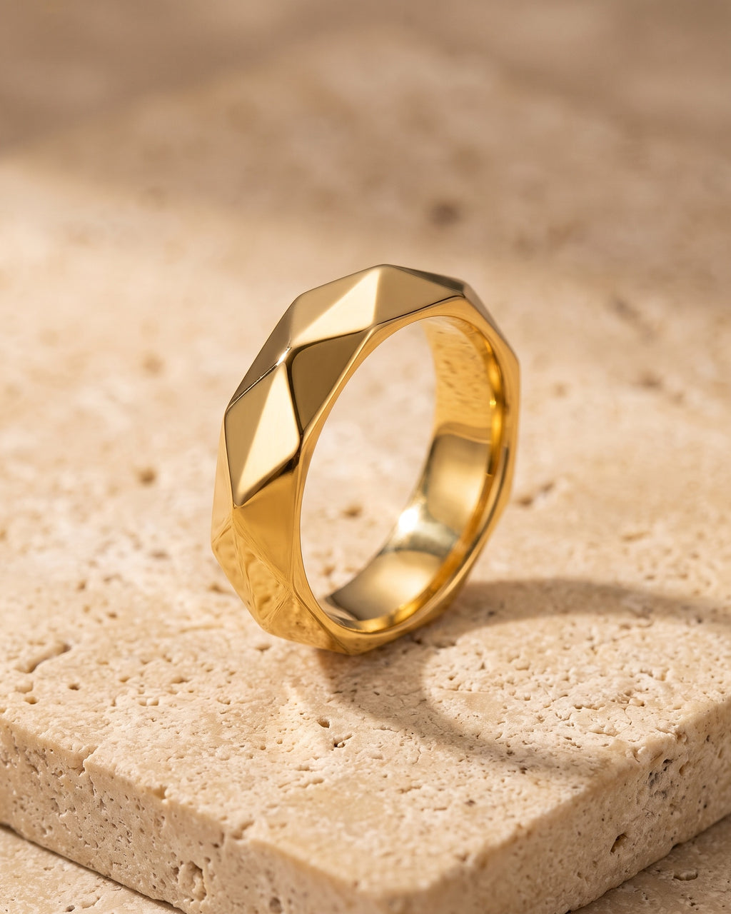 Entire Atlas diamond cut faceted ring in gold-tone steel, lying flat on warm stone