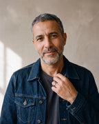 Man in a denim jacket over a charcoal t-shirt by a window wearing the Atlas domed band in silver-tone steel