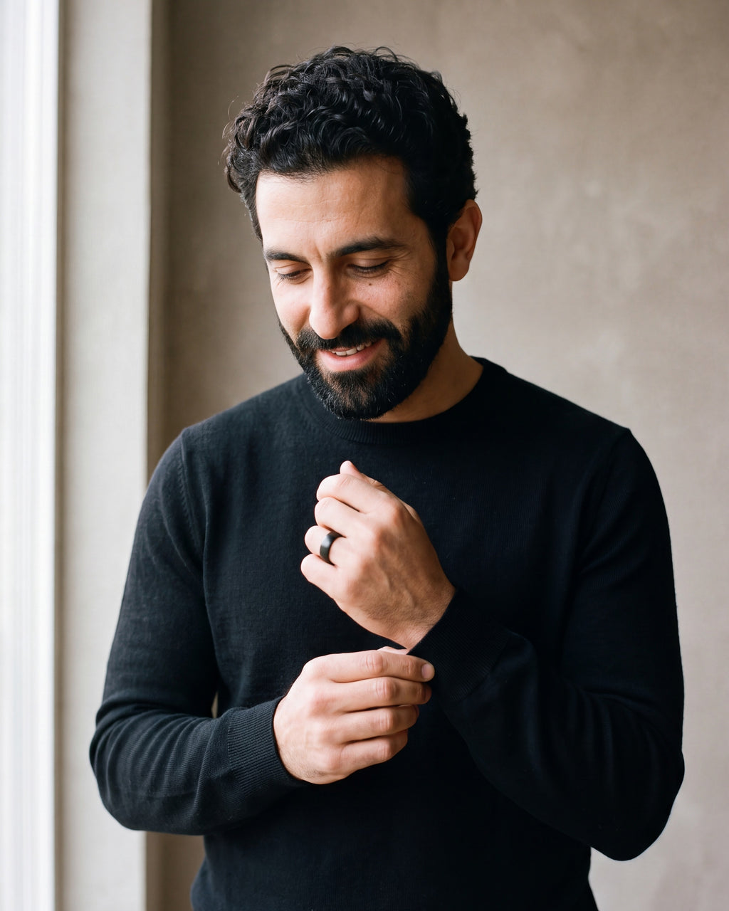 Man in a black sweater adjusting his cuff, wearing the black Atlas domed tungsten ring