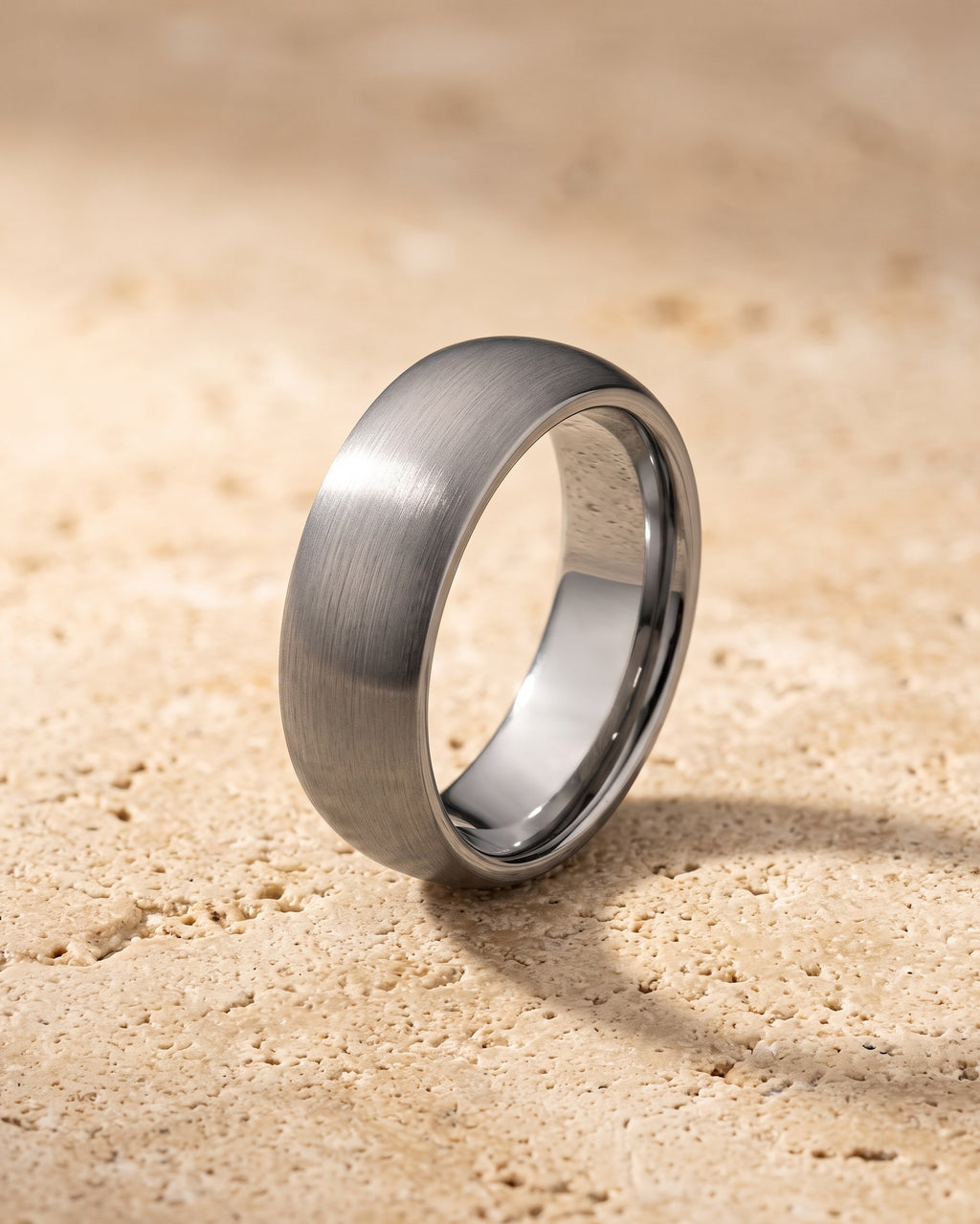 The silver-tone Atlas domed brushed tungsten ring standing on warm stone