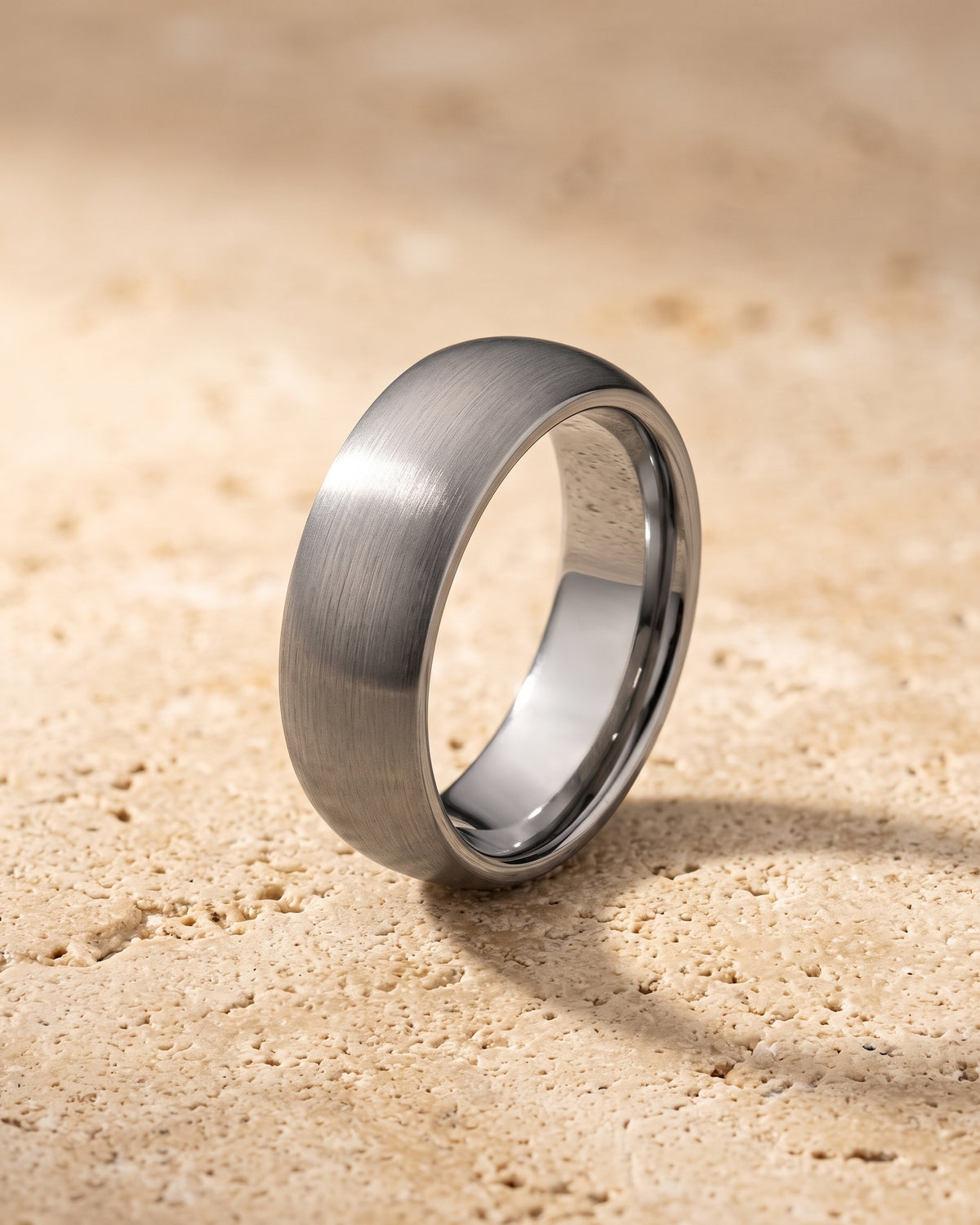 The silver-tone Atlas domed brushed tungsten ring standing on warm stone