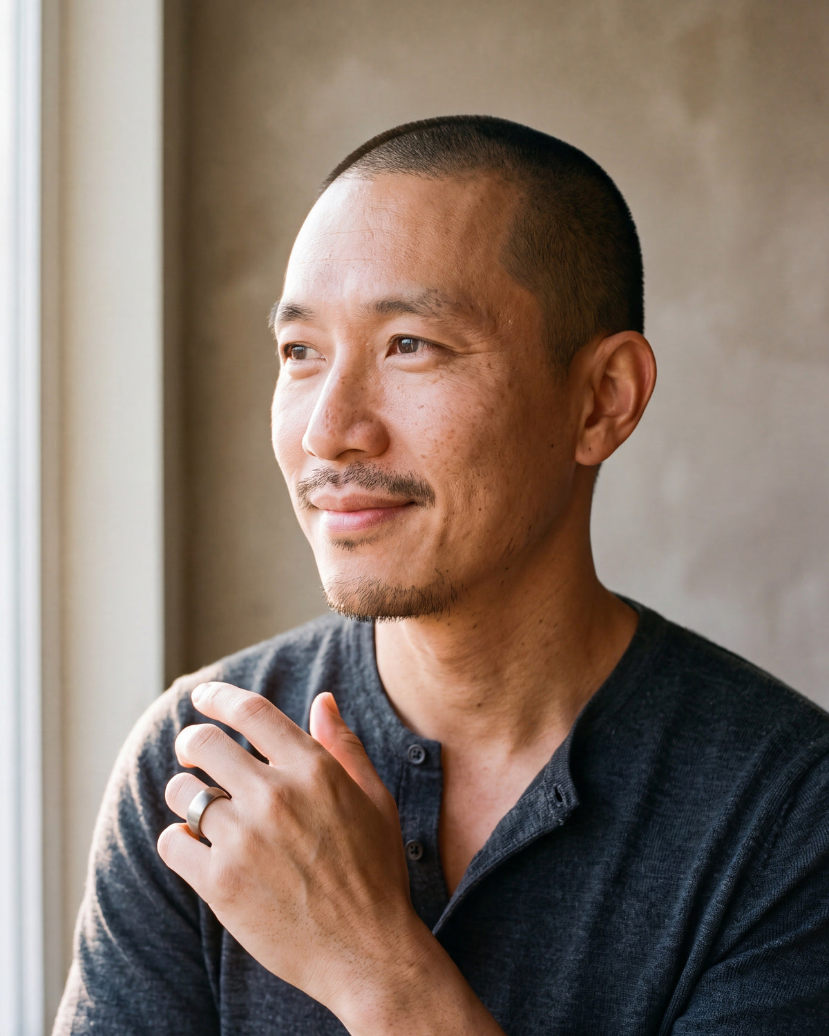 Man in a charcoal henley by a window wearing the silver-tone Atlas domed brushed tungsten ring