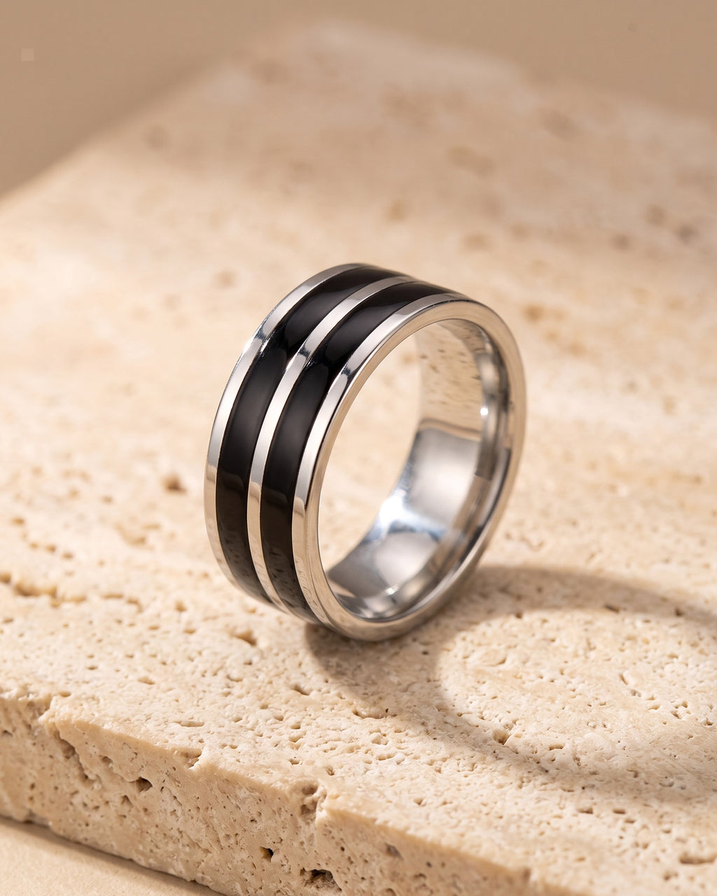 The Atlas double black inlay ring standing on warm stone