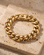 Entire Atlas double-latch Cuban bracelet in gold-tone steel, lying flat on warm stone