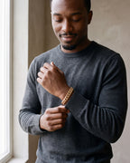 Man in a charcoal knit sweater wearing the Atlas double-latch Cuban bracelet in gold-tone steel
