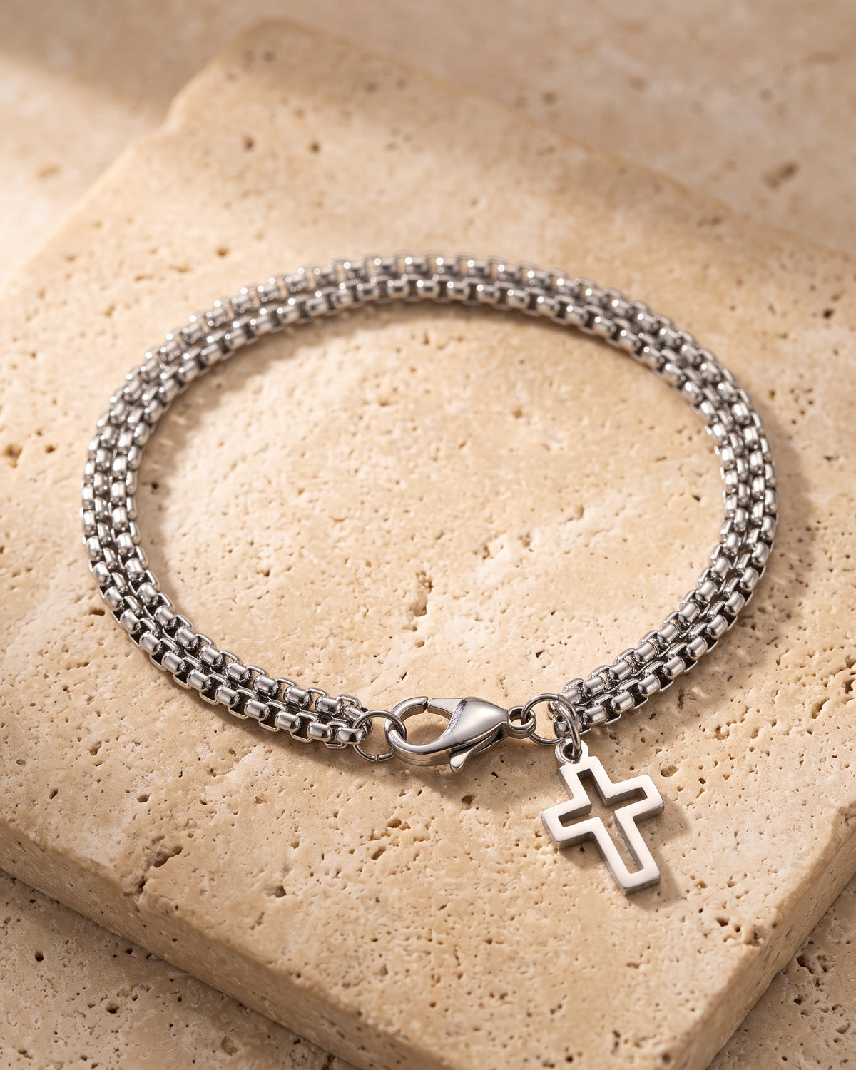 The whole silver Atlas double rolo cross bracelet lying on warm travertine stone