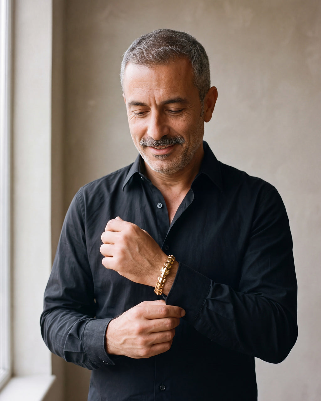 Man in a black shirt adjusting his cuff, wearing the gold-tone Atlas dragon scale bracelet
