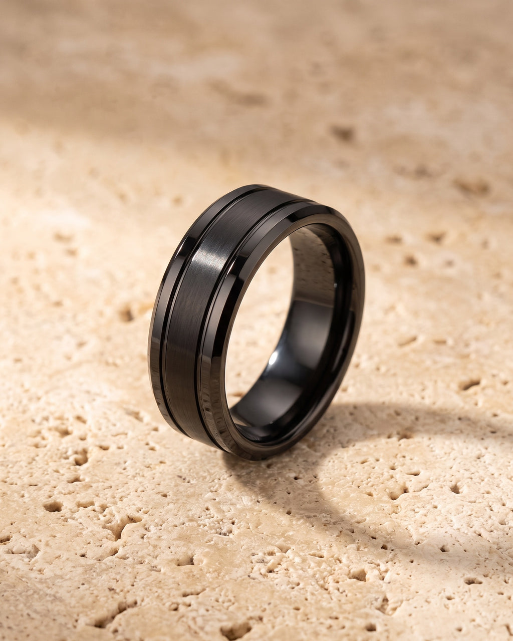 Entire Atlas dual groove ring in black steel, lying flat on warm stone