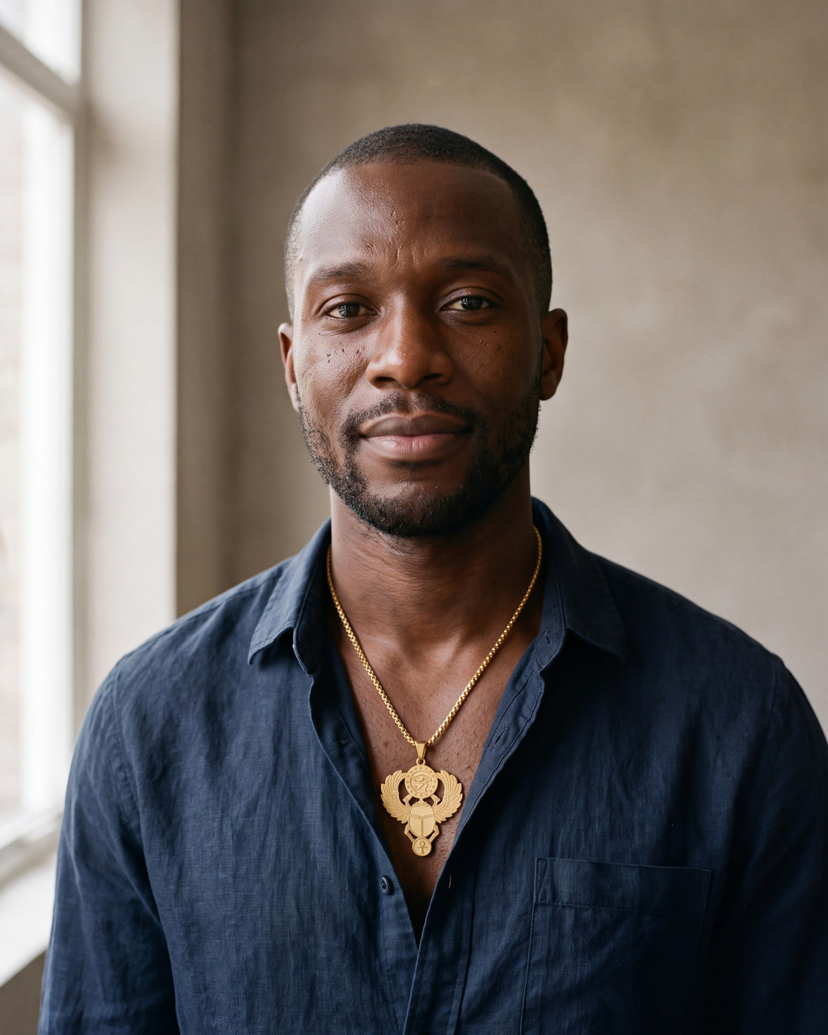 Man in a dark navy linen shirt wearing the gold-tone Atlas Egyptian Scarab Eye of Horus Pendant Necklace