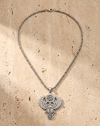 The whole silver-tone Atlas Egyptian Scarab Eye of Horus Pendant Necklace lying on warm travertine stone