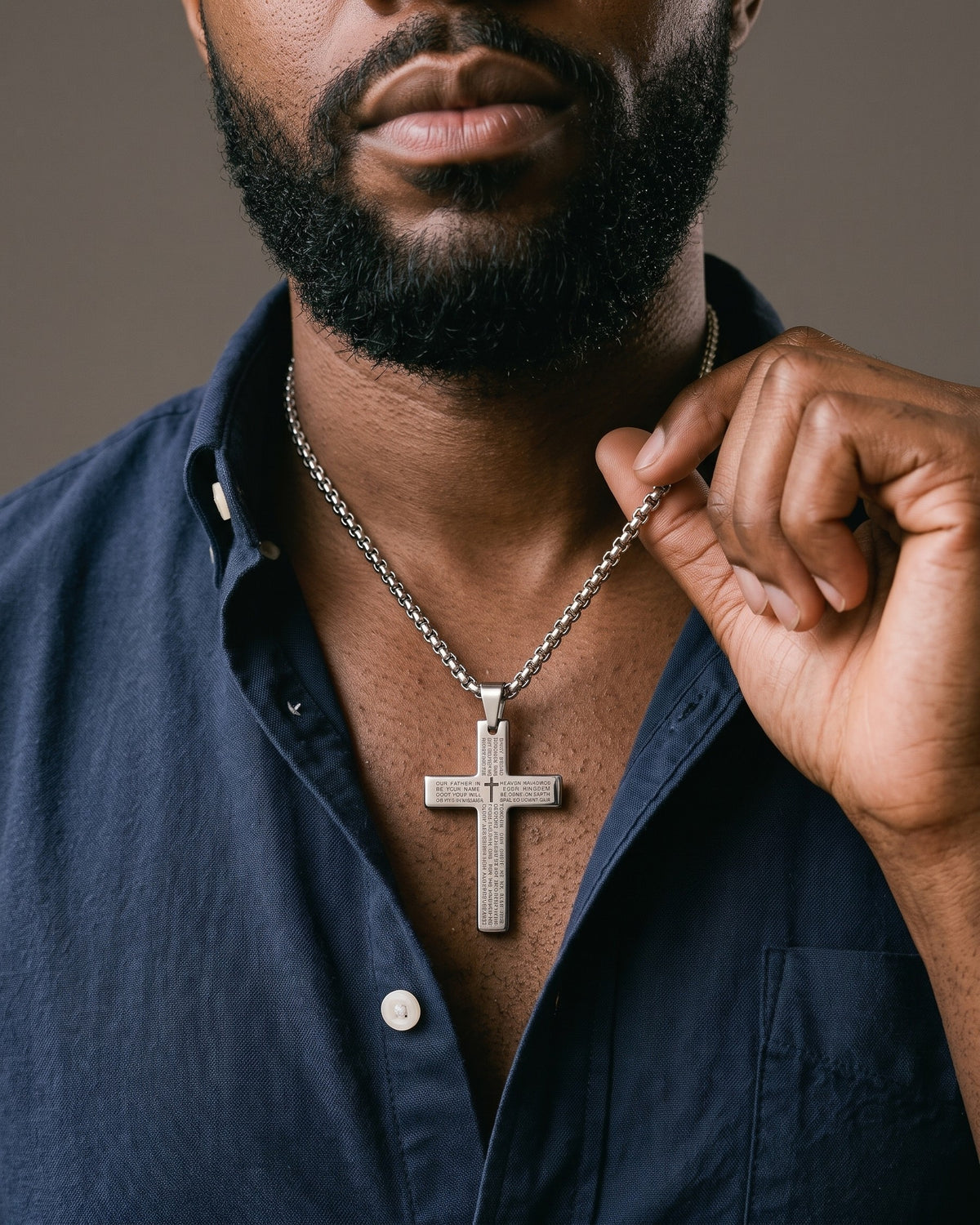 Hand lifting the Atlas Engraved Cross Necklace in Titanium Steel at the collarbone