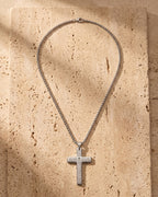 The silver Atlas Engraved Cross Necklace in Titanium Steel laid on warm travertine stone