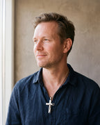 Man in a dark navy linen shirt by a window wearing the silver Atlas engraved crucifix pendant necklace