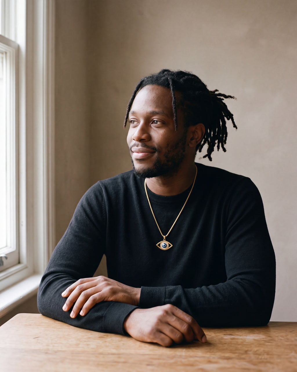 Second man in a black merino crew-neck sweater wearing the gold-tone Atlas evil eye pendant necklace
