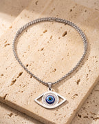 The whole silver Atlas evil eye pendant necklace lying on warm travertine stone