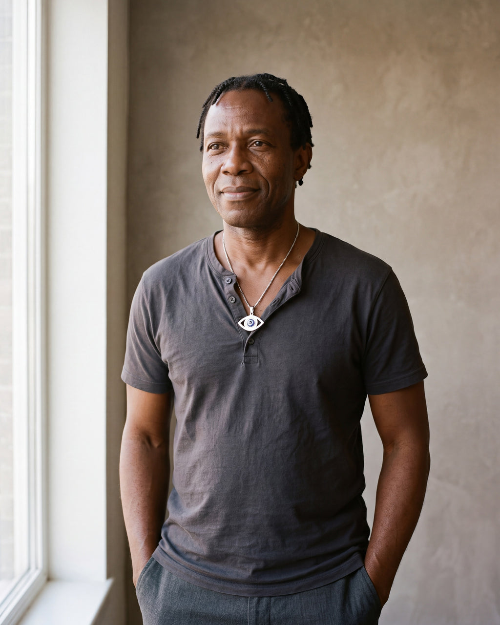 Man in a charcoal cotton henley t-shirt by a window wearing the silver Atlas evil eye pendant necklace