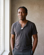 Man in a charcoal cotton henley t-shirt by a window wearing the silver Atlas evil eye pendant necklace