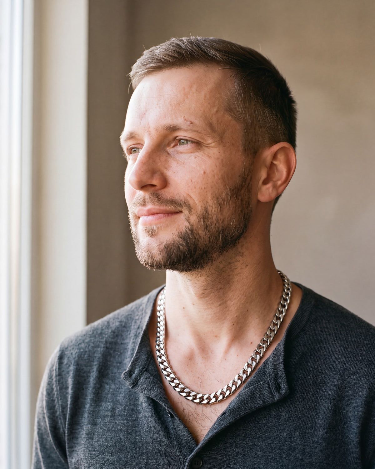 Man in a fine-gauge charcoal-grey merino knit with a henley neckline by a window wearing the silver Atlas faceted double-link cuban chain
