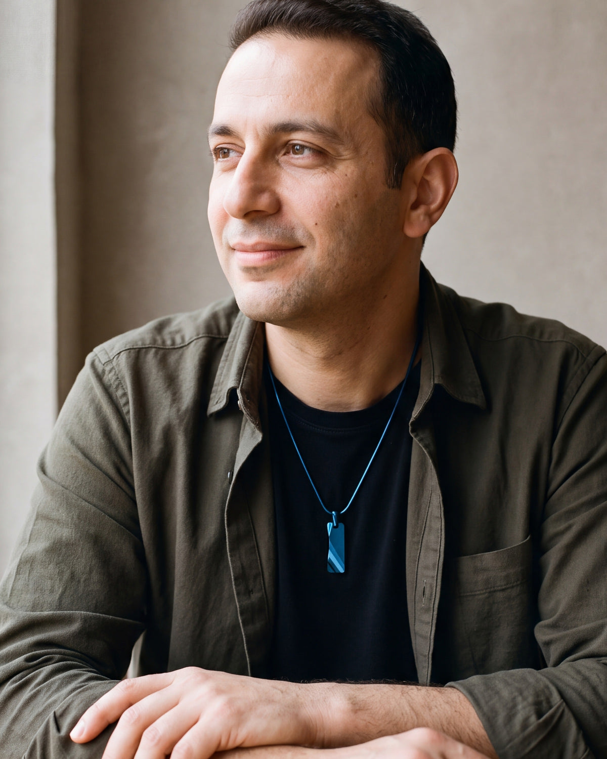 Man in an olive overshirt seated at a table, wearing the blue Atlas faceted tungsten pendant