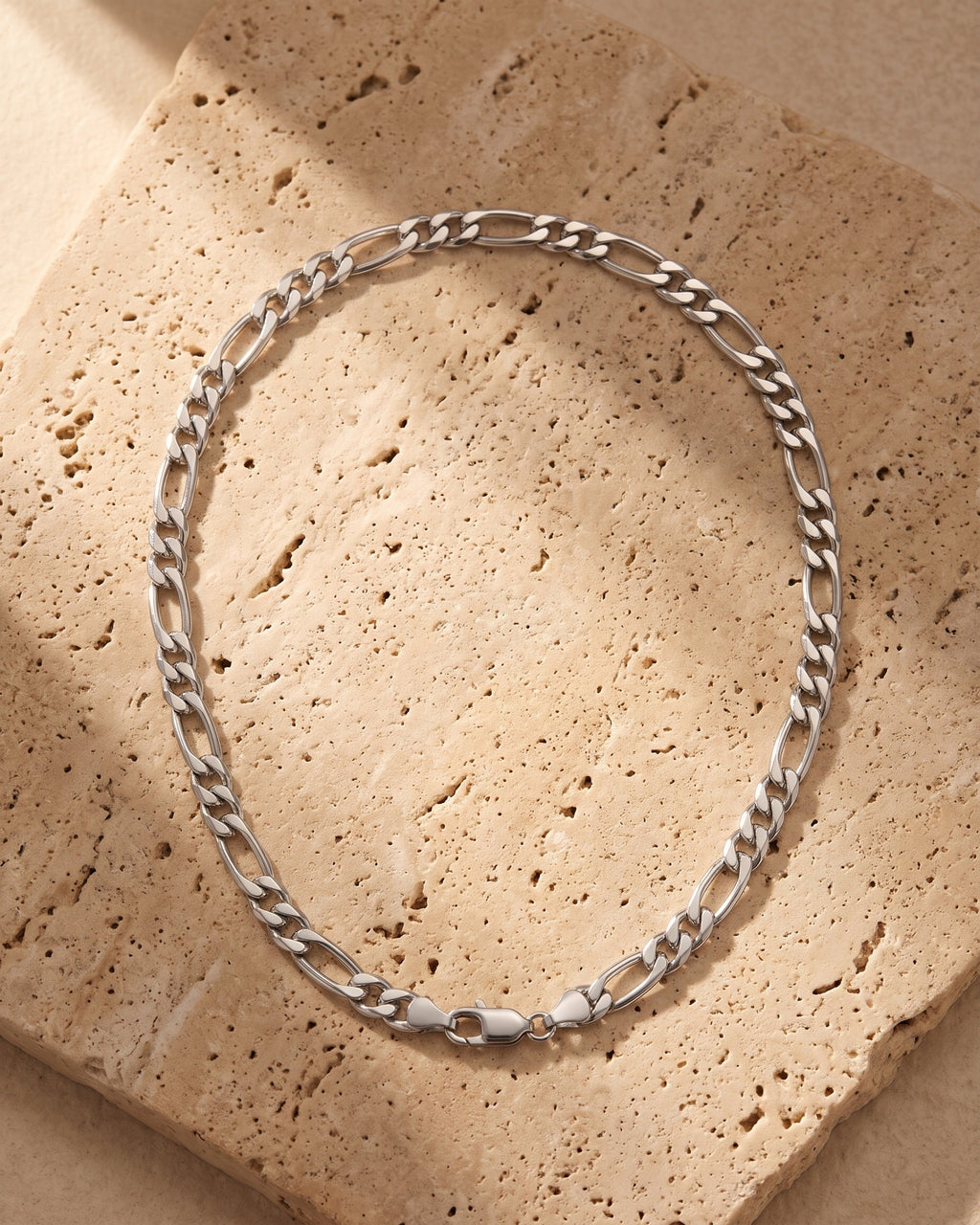 The silver Atlas Figaro Chain in 304 Stainless Steel laid on warm travertine stone