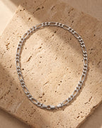 The silver Atlas Figaro Chain in 304 Stainless Steel laid on warm travertine stone