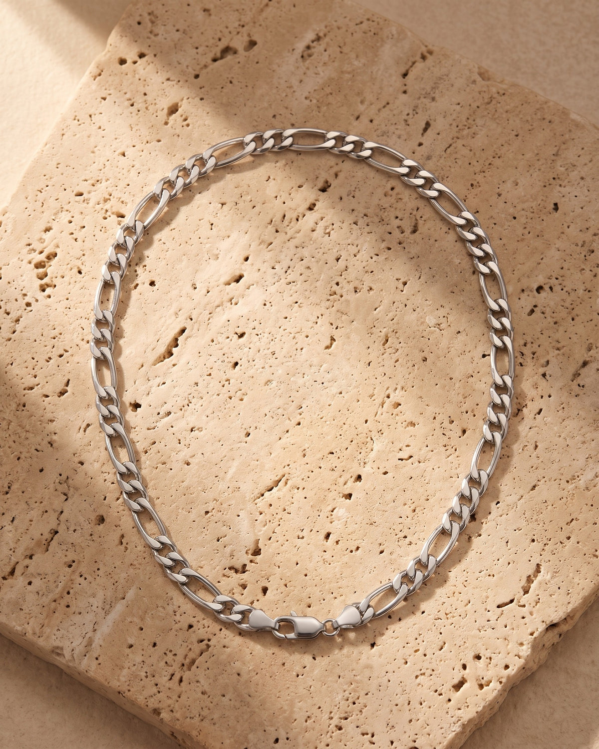 The silver Atlas Figaro Chain in 304 Stainless Steel laid on warm travertine stone