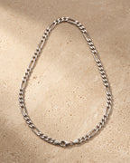 The whole silver-tone Atlas figaro chain lying on warm travertine stone