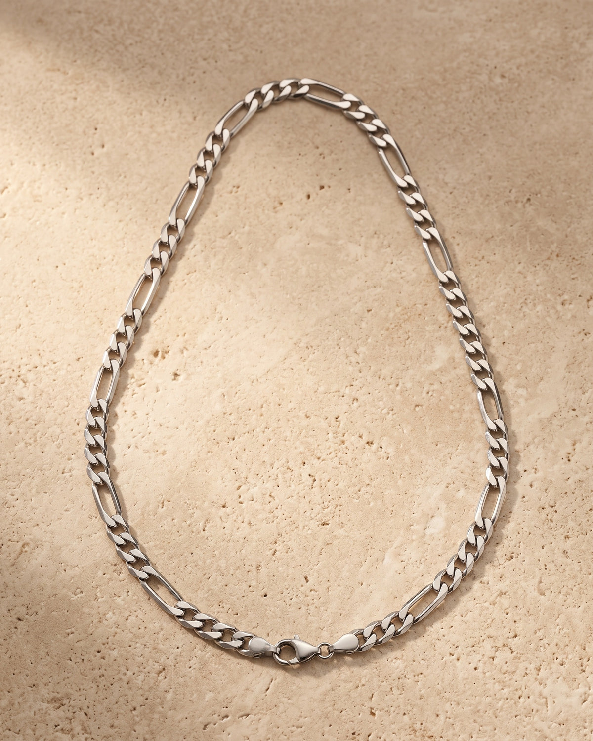 The whole silver-tone Atlas figaro chain lying on warm travertine stone
