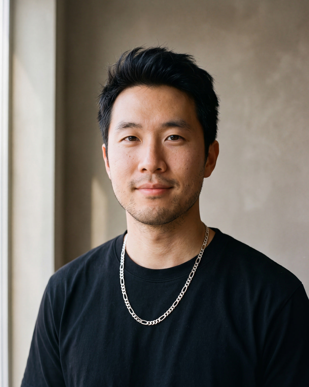 Man in a plain heavyweight black cotton crew-neck t-shirt (thick by a window wearing the silver-tone Atlas figaro chain