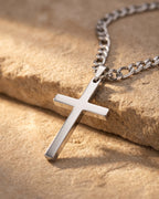 Close-up of the silver-tone Atlas figaro cross pendant necklace resting on warm stone