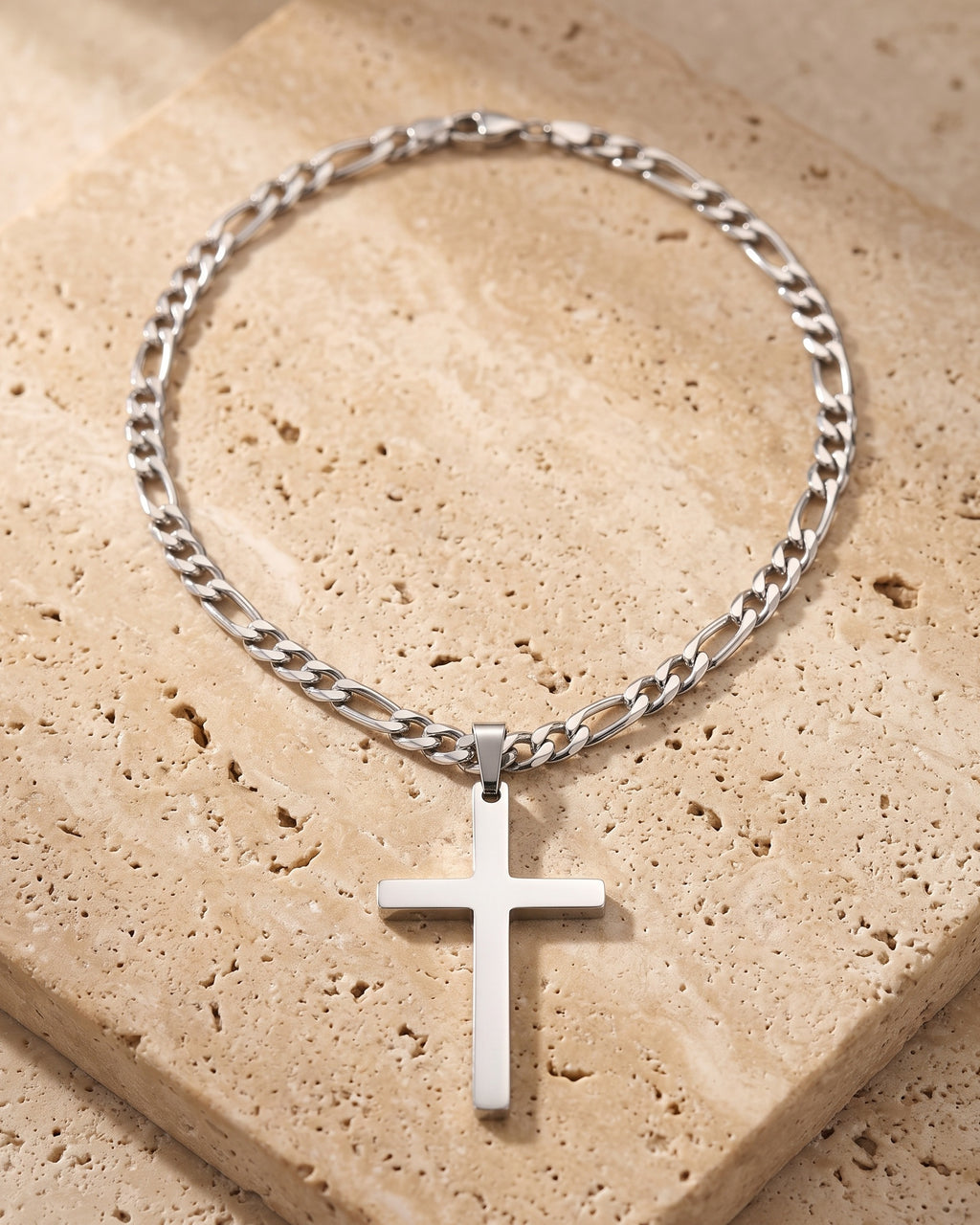 The whole silver-tone Atlas figaro cross pendant necklace lying on warm travertine stone