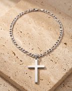 The whole silver-tone Atlas figaro cross pendant necklace lying on warm travertine stone