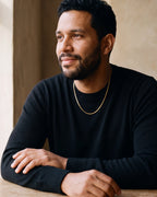 Man in a black sweater seated at a wooden table, wearing the Atlas 1.8 mm gold-tone snake chain