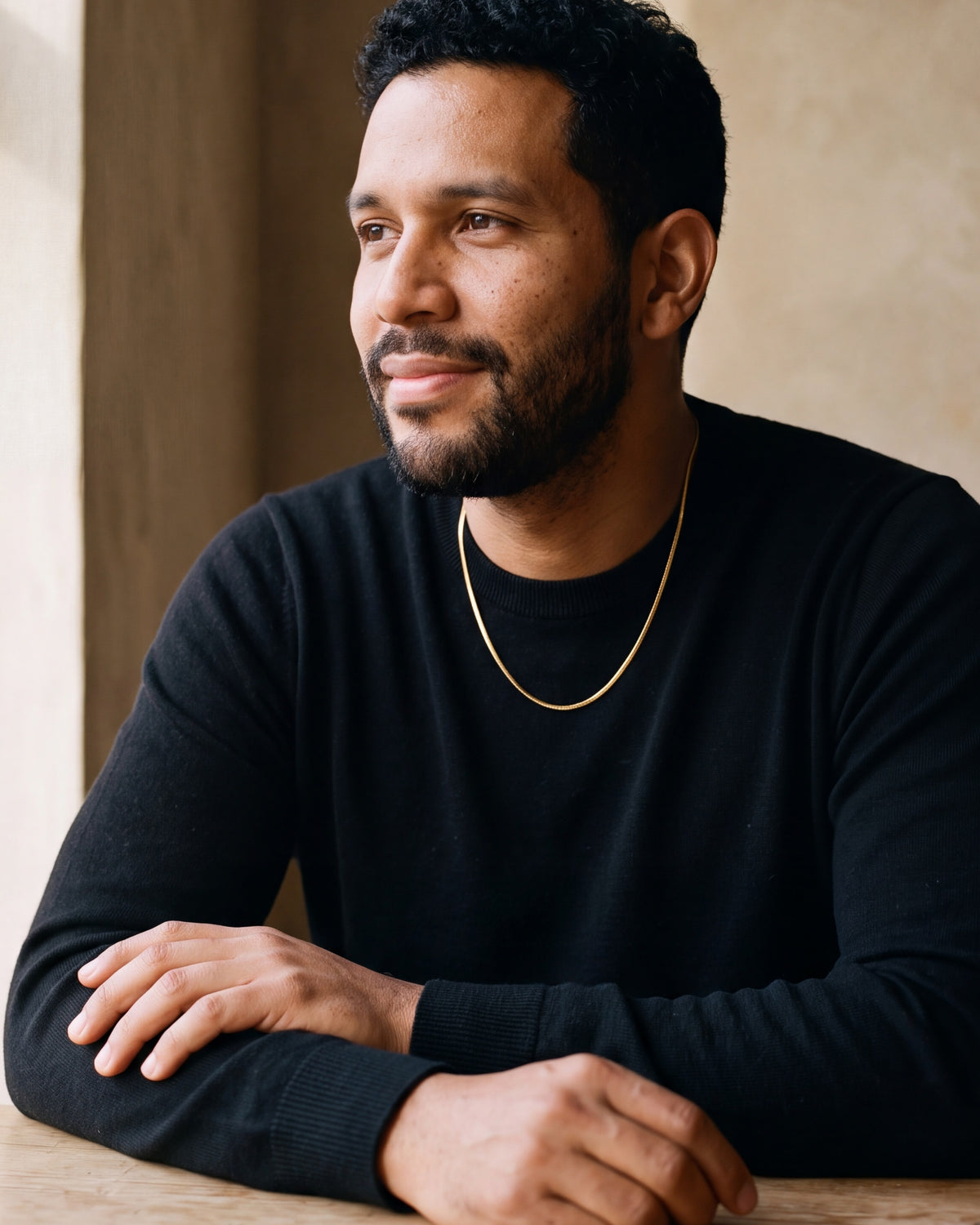 Man in a black sweater seated at a wooden table, wearing the Atlas 1.8 mm gold-tone snake chain